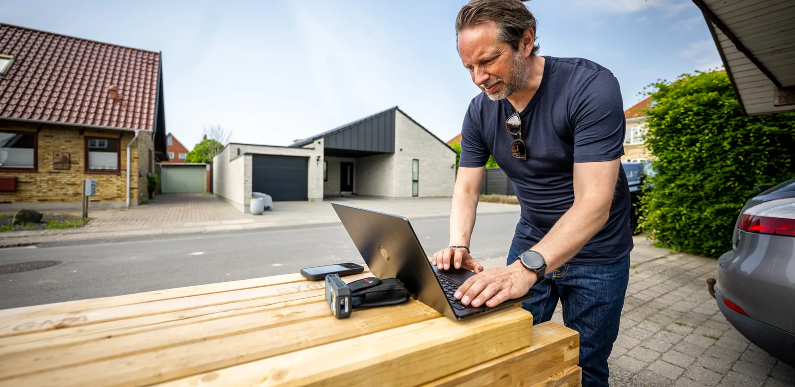 En person arbejder på en bærbar computer ved en stak træ.